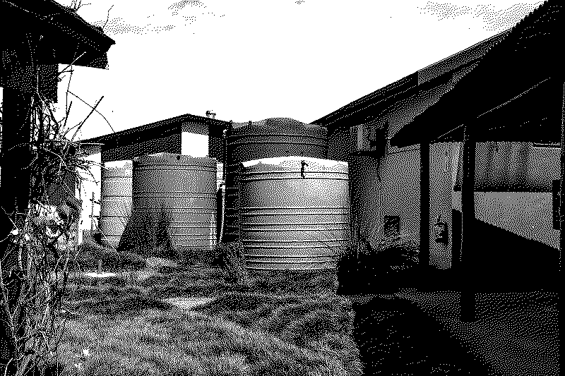 Large ribbed plastic water storage tanks standing on grass between single-storey buildings